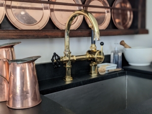 I also have two large soapstone sinks. To coordinate with all the black, I used brass finishes including two Waterworks “Regulator” style faucets. Both have single spouts with black spray nozzles. I also display many pieces from my copper collection in this kitchen.