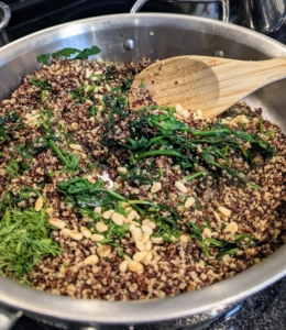 She adds the quinoa, dill and pine nuts to the pan and mixes them together.