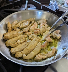 The chicken is cooked through in a skillet with two tablespoons olive oil over medium-high heat. This takes about four-minutes per side. Afterwards, it is transferred into the bowl with the marinade and set aside.