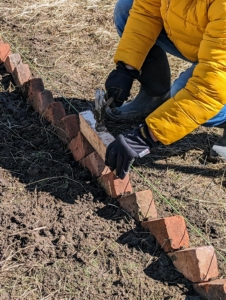 Fernando follows behind and uses a scrap piece of wood on top of the bricks to pound them securely in place. The wood protects the bricks from getting damaged in the process.