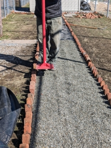 And then pressed down with a gravel tamper. A tamper is a tool with a long handle and a heavy, square base used for leveling and firmly packing gravel, dirt, clay, sand, and other similar materials.