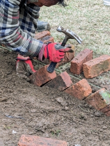 Pete uses the end of the hammer to gently tap the brick into place. In time, the soil will fill in any gaps and keep the bricks secure.