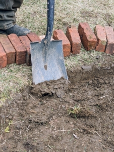 Once again, Pete removes the grass and some soil along the line, creating a narrow trench just wide enough for the bricks and about five inches deep.