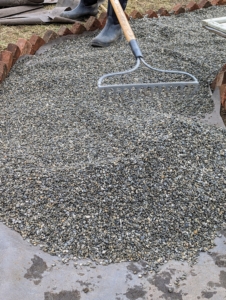The gravel is spread evenly with a hard rake. Afterwards, Fernando will go over it with a gravel tamper. A tamper is a tool with a long handle and a heavy, square base used for leveling and firmly packing gravel, dirt, clay, sand, and other similar materials.