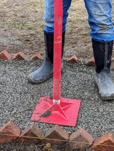 Afterwards, Fernando goes over it with a gravel tamper. A tamper is a tool with a long handle and a heavy, square base used for leveling and firmly packing gravel, dirt, clay, sand, and other similar materials.