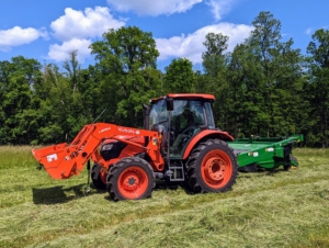 Chhiring hooks up the mower-conditioner to our trusted Kubota M4-071 tractor. Chhiring is now in the cab of the tractor ready to cut. The process of cutting should take about an hour.
