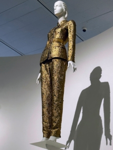 This suit in a shimmering bronze color is from House of Chanel, autumn/winter 1996–97. Lagerfeld made designs that were both luxurious as well as everyday - this shows the combination of both styles.