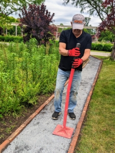 Afterward, Fernando goes over it with a gravel tamper. A tamper is a tool with a long handle and a heavy, square base used for leveling and firmly packing gravel, dirt, clay, sand, and other similar materials such as the stone dust.