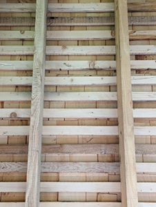 From the inside of the coop looking up, one can see the horizontal slats on one side along with the shingles that are secured to the slats.