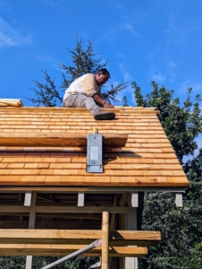And here he is working on the ridge of the roof. The roof ridge is the horizontal line running the length of the roof where the two roof planes meet. This intersection creates the highest point, sometimes referred to as the peak.