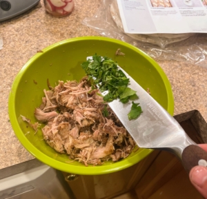 ... and then breaks the pork up into bite sized pieces. Here, he is adding half of the cilantro.