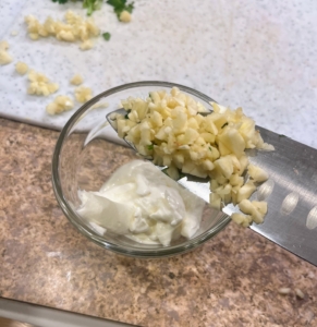 To make the toppings, Brian puts the sour cream in a bowl, thins it with a little water, and then stirs in the chopped garlic along with some salt and pepper to taste.