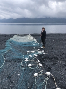 Here is Hannah on the beach with the giant net used for harvesting fish at the set net site. She often lays out the entire net, checks it, and does any mending if necessary. (Photo courtesy of Hannah Heimbuch)