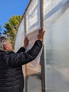 Any vents on my hoop houses are also covered. Fernando measures the industrial strength plastic that will cover the vent slats.