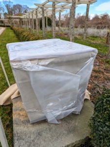 By lunchtime, Pete and Fernando are working along the carriage road next to my winding pergola. Here is one of six giant square stone planters I purchased earlier this year. First it is carefully covered in plastic.