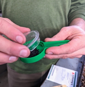 After pouring a generous amount of seeds into the center dish, Ryan screws the plastic top back onto the hand seed sower and adjusts the amount of seeds that will be released at one time.