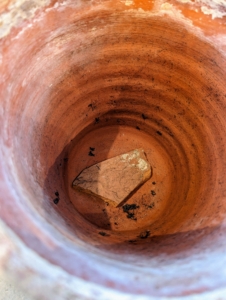 A clay shard is placed over the hole to help with drainage. We always save shards from broken pots – it’s a great way to repurpose those pieces.