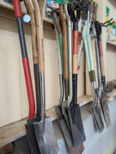 We use industrial hooks that can hold up to 50-pounds each. We keep like items together, so we know where to find them and how many we have in supply. Here are some of our shovels and spades. Do you know the difference between a shovel and a spade? A shovel is longer, angled, and its blade is curved into more of a scoop with a pointed tip. Shovels are better for digging up, breaking apart, and lifting soil as well as for scooping and moving loose materials. A spade has a relatively flat blade with straight edges and the blade tends to be in line with the shaft, rather than angled forward. Spades are good for edging and cutting.