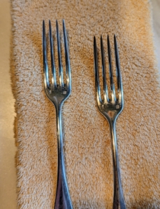 Here on the left is a polished fork, and on the right is one that still needs polishing. It is hard to see, but there is a slight discoloration. Tarnish is caused when the chemical element of silver reacts with hydrogen sulfide, which occurs naturally in the air. This produces silver sulphate on the surface of the silver and shows up as the common black-brown tint.