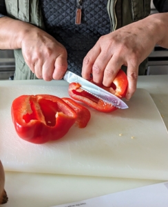 The first step is to prep the ingredients, or mis en place, a French culinary phrase which means "putting in place" or "gather". It refers to any setup needed before cooking. Here, Elvira removes the core and seeds from the bell pepper and cuts first in half, then into smaller pieces...