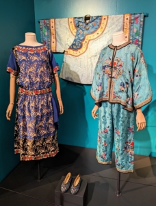 The Chinese embroidered silk outfit on the right belonged to poet Edna St. Vincent Millay. They show her fondness for different cultures and styles. On the left, an American made garment featuring the influence of Chinese patterned textiles. This dress could have been worn in the afternoon or for dinner.