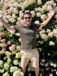 Outside, Ryan is standing in front of a large display of hydrangeas featuring three varieties - "Vanilla Strawberry," "Berry White," and First Editions "Little Hottie."