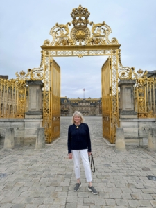 Gilded gates with the Sun King and spider webs guard the entrance to Versailles.