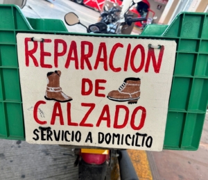 This sign is on the back of a motorcycle - a traveling shoe repairman.