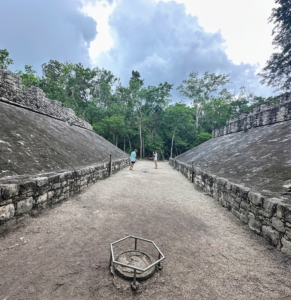 This is a Mayan ball court where the the ancient game of Pok-A-Tok was played. The court features a long trench area with vertical sloping walls on each side and two stone rings where "goals" were scored. Two teams of seven athletes would compete in this vicious yet ritualistic sacred game, kicking a ball with their hips, elbows, knees, and forearms so as to keep it from falling. Only the best warriors of the community could participate.