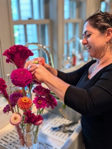 Next, Enma works on an an arrangement of dark pink to burgundy colored blooms. One can stick to like colors when arranging to find complementary colors. This arrangement includes the zinnias, cosmos, and celosias.