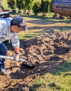 Phurba follows to remove any excess soil and manually smooths out the trench as needed.