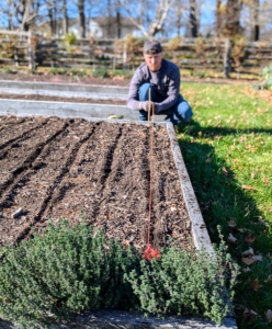 Josh secures twine to ensure the rows are perfectly straight. This is a guide for all the other rows in the bed. Ryan already determined how many rows would fit in this bed and how many garlic cloves would be planted in each row.