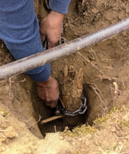 Pete secures one end of a chain to the piece stuck in the hole and the other end to the bar.