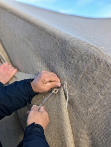 At the ends, Phurba pulls the burlap snug and begins sewing it closed. For this he uses a large embroidery needle and jute twine.