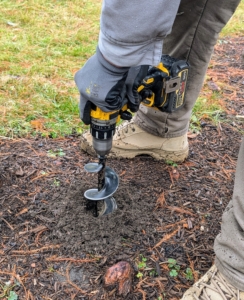 Close by, Ryan uses the auger attachment to make holes. The ground is a bit hard from the recent cold, but it's still workable.