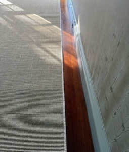 Because the carpet is cut slightly smaller than the space to expose the wood floors, the area between the carpet edges and the walls must be measured several times. This carpet is about four-and-a-half inches from the wall along every side.