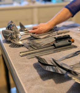 When organizing kitchen utensils, the first thing to do is place everything on a table and group like items together, discarding any that are broken or too worn.