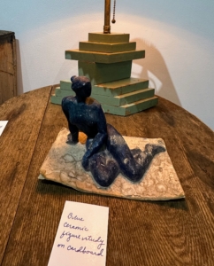 On this handmade wooden table - a blue ceramic sculpture of a woman on cardboard.