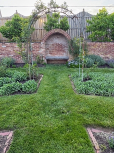 In this corner is a bench in a nook built into the wall of the Rose Garden. The arch features Rosa 'New Dawn'.