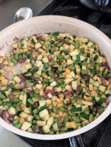 To the same skillet, Enma adds the zucchini, corn and edamame, or young soy beans. Enma seasons with salt and pepper and cooks them while stirring until the vegetables are softened.