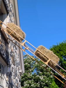 The crew sets up the hay elevator to the hay loft. Then each bale is placed on the hay elevator which sends it up to waiting hands. Baling hay is a team effort. Each bale is about 15 by 18 by 40 inches large. The number of flakes in the bale is determined by a setting in the baler. Many balers are set for 10 to 12 flakes per bale.