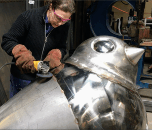 Here she is grinding and attaching pieces of steel to the body. Looking closely, one can see her drawings on the metal. Every piece is attached so carefully and precisely.