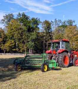 Behind him is a rake that picks up the cut and dried hay and rakes it into windrows that can be baled.