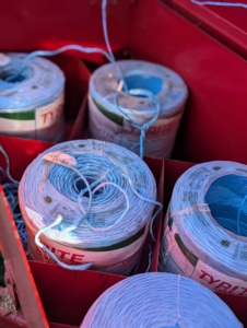 Large rolls of twine are positioned and tied to each other, so they can feed into the baler and secure the hay just before it shoots out into the trailer.