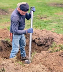 Alex continues the hole digging started by the backhoe.