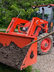 Another bucket full of mulch is carried to its location. These buckets can be lowered to ground level or raised high while in motion.