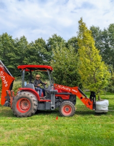 I am very fortunate to have Kubota tractors. They are used for a multitude of tasks all year long. This one is the M62. It is equipped with a forklift, a front loader, and a backhoe. On this day, the tractor is transporting one of many European hornbeams, Carpinus betulus ‘Frans Fontaine,’ to its planting location.