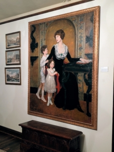 This is a family portrait of Lucie Bigelow Rosen and her children, Walter and Anne. This was painted in their New York City townhouse and is now displayed at Caramoor along with the green desk in the painting.