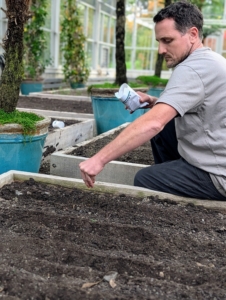 Ryan drops seeds carefully in the bed. These raised beds were designed for easy reach from all sides, so that work can be done quickly and efficiently.