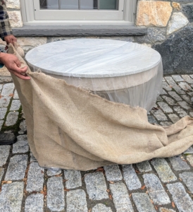 When we can, we reuse burlap from seasons past; however, it is also available in giant rolls of 40-inches or 60-inches wide. Also called hessian, burlap is made in Pakistan, Bangladesh and India from jute, a tall, grass-like plant grown for its strong fibrous stalks. This burlap cover is from last year. If stored properly in a dry place, it can last a couple of seasons. Pete wraps this entire vessel from top to bottom with the burlap, tucking it all in underneath.